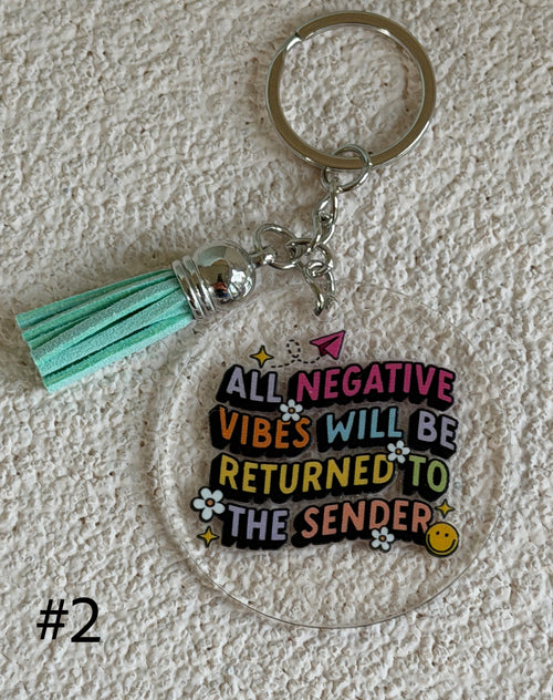 A clear acrylic keychain with a mint green faux-leather tassel and a silver metal key ring. The acrylic charm features the text 'ALL NEGATIVE VIBES WILL BE RETURNED TO THE SENDER' in colorful bubble letters with small decorative doodles.