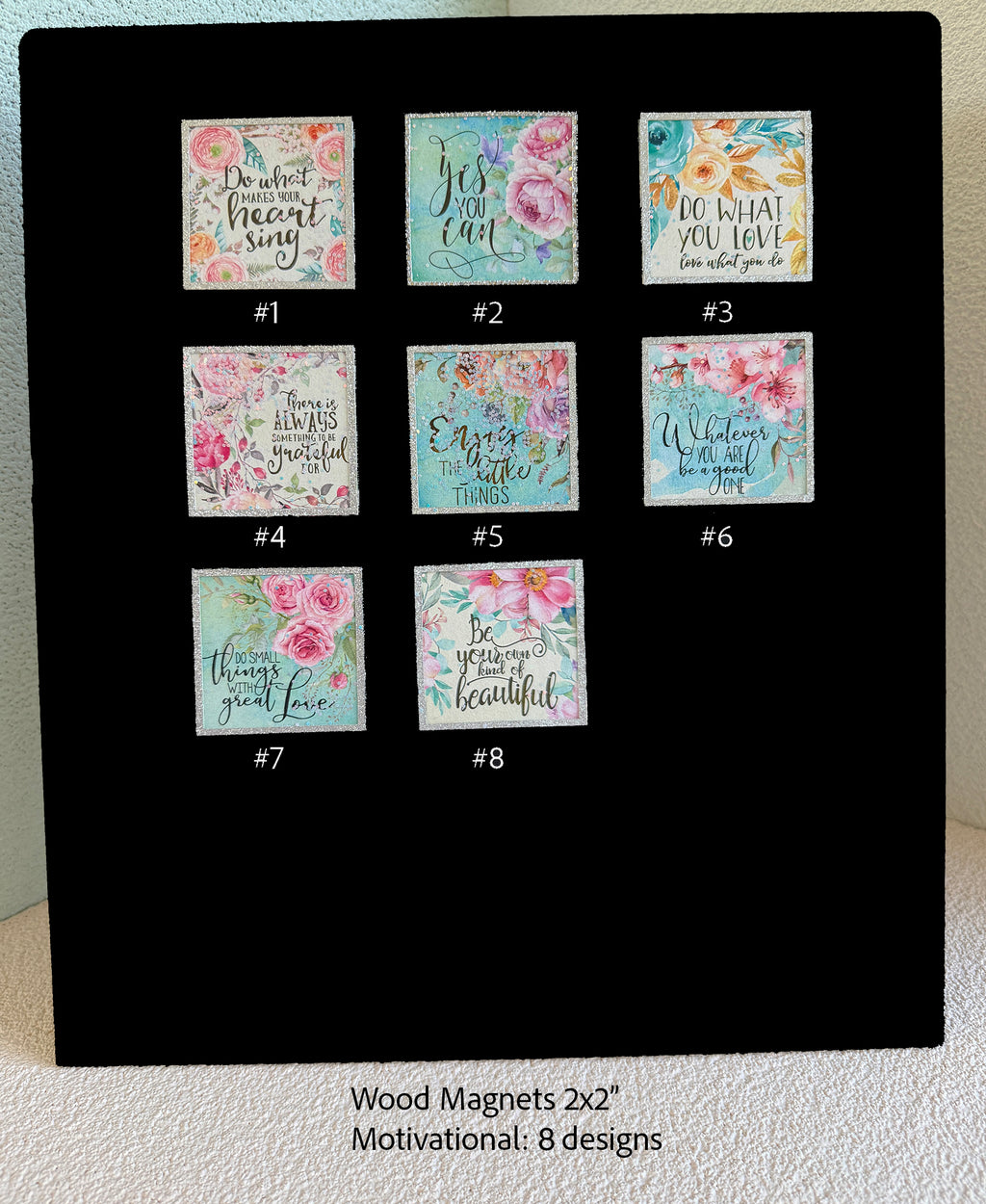 A black display board showing eight small floral motivational wood magnets labeled #1 through #8, with text below reading 'Wood Magnets 2x2" Motivational: 8 designs'.